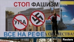 Ukraine -- A man pastes another poster over one calling for people to vote against fascism in an upcoming referendum in the Crimean port city of Sevastopol, March 10, 2014