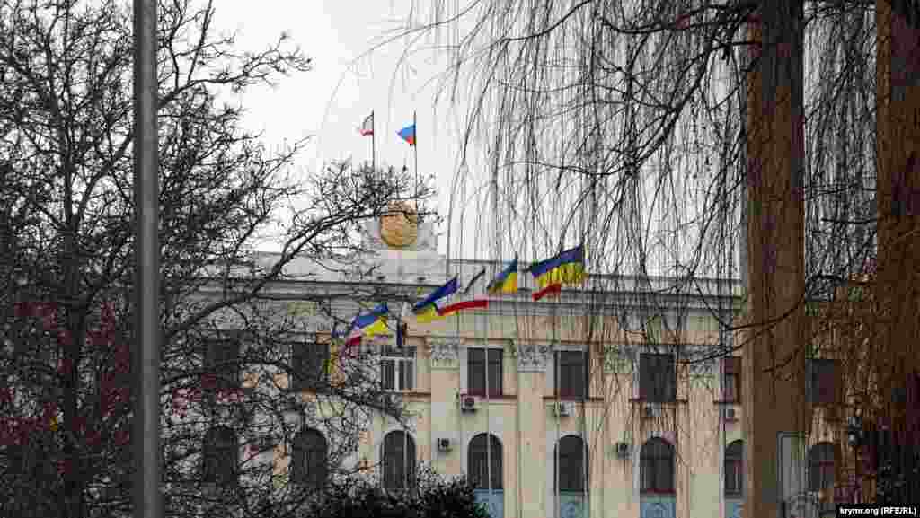 Последние украинские флаги в городе. &laquo;Ополченцы&raquo; бы их давно сорвали, но флагштоки стоят перед зданием Совета министров, в зоне оцепления, куда не пускает милиция. А &laquo;зеленые человечки&raquo; пока из Совмина и Верховной Рады так и не выглянули. В этот день, в пятницу, &nbsp;администрация школ в центре Симферополя &nbsp;рекомендовала школьникам пропустить занятия. Не приказала, а именно рекомендовала Это был последний день зимы 2014 года.